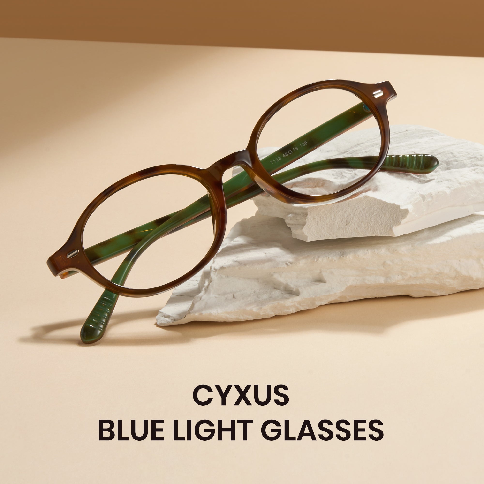Brown eyeglasses with green accents on a beige surface, featuring the brand 'CYXUS'.