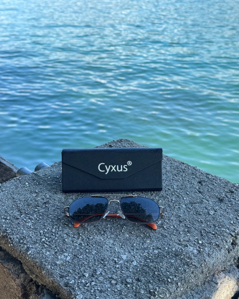 Cyxus sunglasses P1021 and case on a rock with water in the background