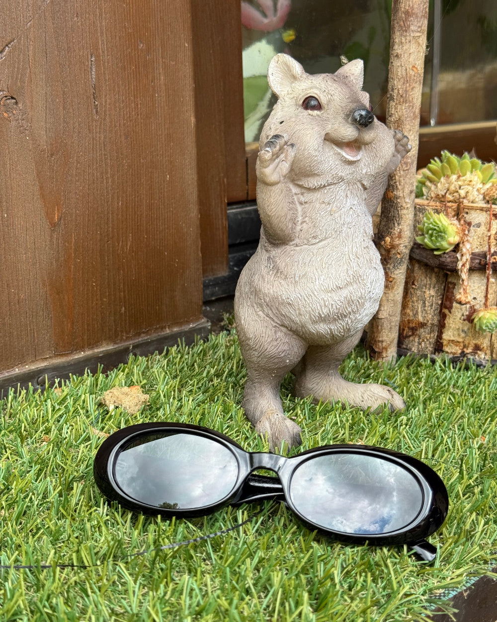 Stone sculpture of a squirrel and a pair of black-framed sunglasses on grass.