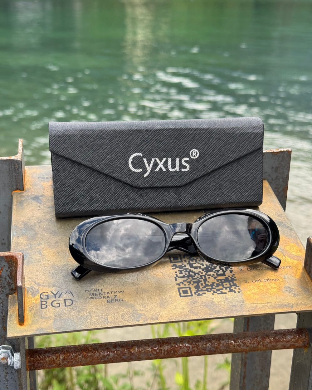 Cyxus sunglasses and case on a metal surface with a blurred natural background