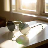 Gold-framed sunglasses on a reflective surface with a window in the background