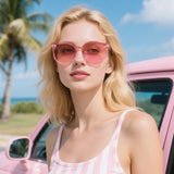 Woman wearing pink sunglasses and a striped tank top in front of a pink car with palm trees and blue sky in the background.