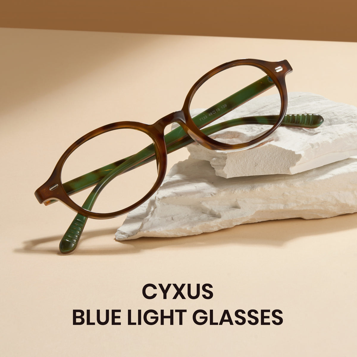 Brown eyeglasses with green accents on a beige surface, featuring the brand 'CYXUS'.