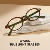 Brown eyeglasses with green accents on a beige surface, featuring the brand 'CYXUS'.