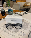 Cyxus smart glasses 8284 on a newspaper with a white box labeled 'Smart Glasses' in a casual setting.