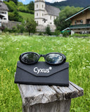 Cyxus polarized sunglasses on a black case with a scenic background of a church and mountains.