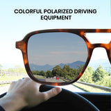 Sunglasses held up to a car windshield with a scenic road and mountains in the background